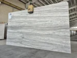 Marjan Silver Travertine slab with flowing silver-gray veins suspended from a lifting clamp.